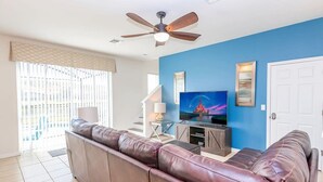 Ein Wohnzimmer mit braunem Ledersofa, Deckenventilator, Fernseher und einer Treppe, die zu einer oberen Etage führt.