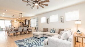 Una sala moderna con sofá modular, comedor, cocina y ventilador de techo.