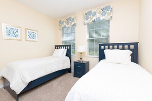 A bedroom with two single beds, a nightstand with a lamp, and two framed pictures on the wall. - Private Pool, Spa & Game Room Near Disney Parks (Kissimmee)