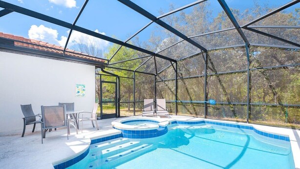 Et overdækket swimmingpool med jacuzzi, omgivet af en metalramme, og en terrasse med stole og et bord.