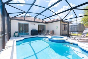 An indoor swimming pool with a glass ceiling, a barbecue area, and a patio with chairs. - Private Pool, Spa & Game Room Near Disney Parks (Kissimmee)