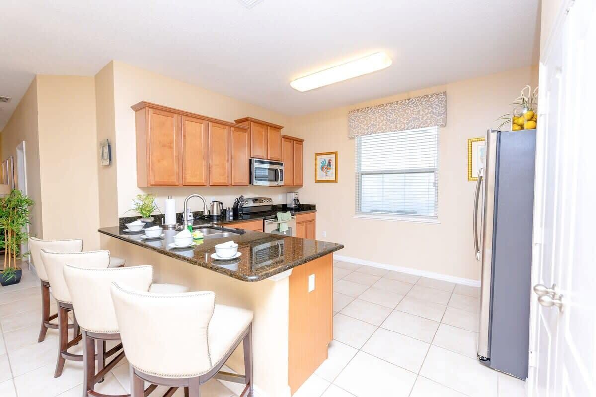 A kitchen with wooden cabinets, a central island with bar stools, a refrigerator, and a microwave.