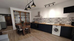 A modern kitchen with a dining area, a washing machine, and a TV mounted on the wall. - Gîte de L'atelier (Saint-Privat)