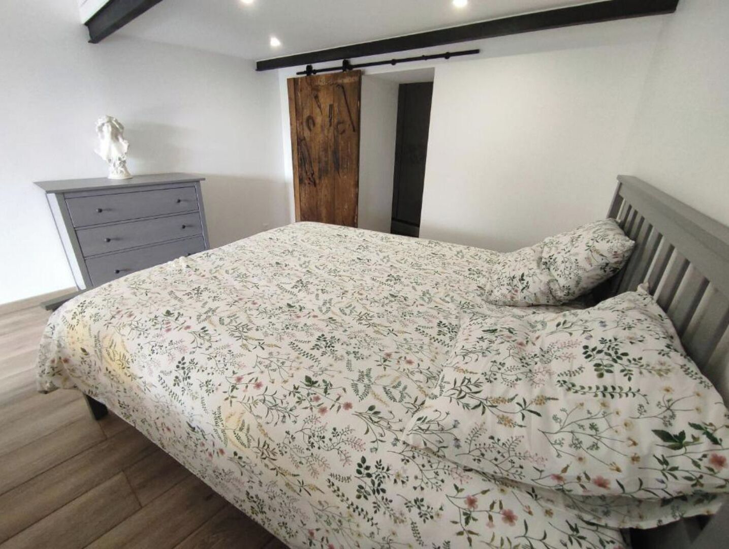 A bedroom with a floral bedspread, a grey dresser, and a wooden door.