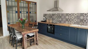 A kitchen with a wooden table, blue cabinets, and patterned backsplash. - Gîte de L'atelier (Saint-Privat)