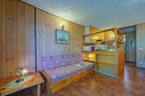 Interior em madeira com um sofá, uma mesa com abajur e uma estante.