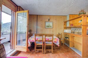 A room with a dining table, chairs, a kitchen area, and a sliding glass door leading to a balcony. - Appartamento Bareu Mountain View (Sauze d'Oulx)