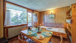 Una habitación acogedora con paredes de madera, una mesa de comedor dispuesta con platos, tazas y una cafetera, y una cama con cabecera estampada.