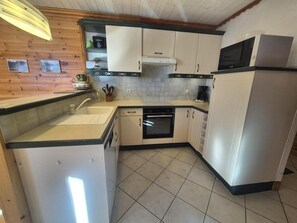 Uma cozinha compacta com armários brancos, forno embutido, micro-ondas e pia.