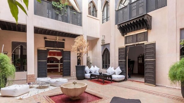 Un patio con mobiliario exterior, una fuente decorativa y un edificio de arquitectura tradicional marroquí.