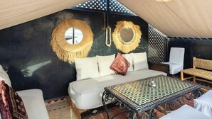 Un espacio al aire libre acogedor, con asientos en tienda de campaña, un sofá blanco, una mesa con estampado y decoraciones de pared tejidas.