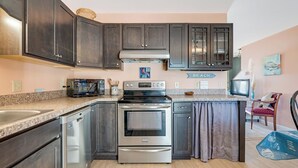 A kitchen with dark cabinets, stainless steel appliances, a granite countertop, and a sign that says 'BEACH.' - The Mermaid Lounge by Seaside Vacations & Sales (Chincoteague Island)