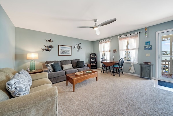 A living room with a sofa, coffee table, and a dining area with chairs and a table. - The Mermaid Lounge by Seaside Vacations & Sales (Chincoteague Island)