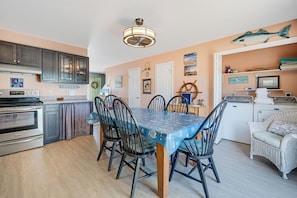A kitchen with a dining area, featuring a table with chairs, a refrigerator, and a sink. - The Mermaid Lounge by Seaside Vacations & Sales (Chincoteague Island)