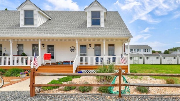 A two-story house with a covered porch, a flag, and a small garden area. - The Mermaid Lounge by Seaside Vacations & Sales (Chincoteague Island)