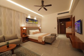 A hotel room with a bed, a sofa, a TV, and a ceiling fan. - Mars Resorts (Meerut)