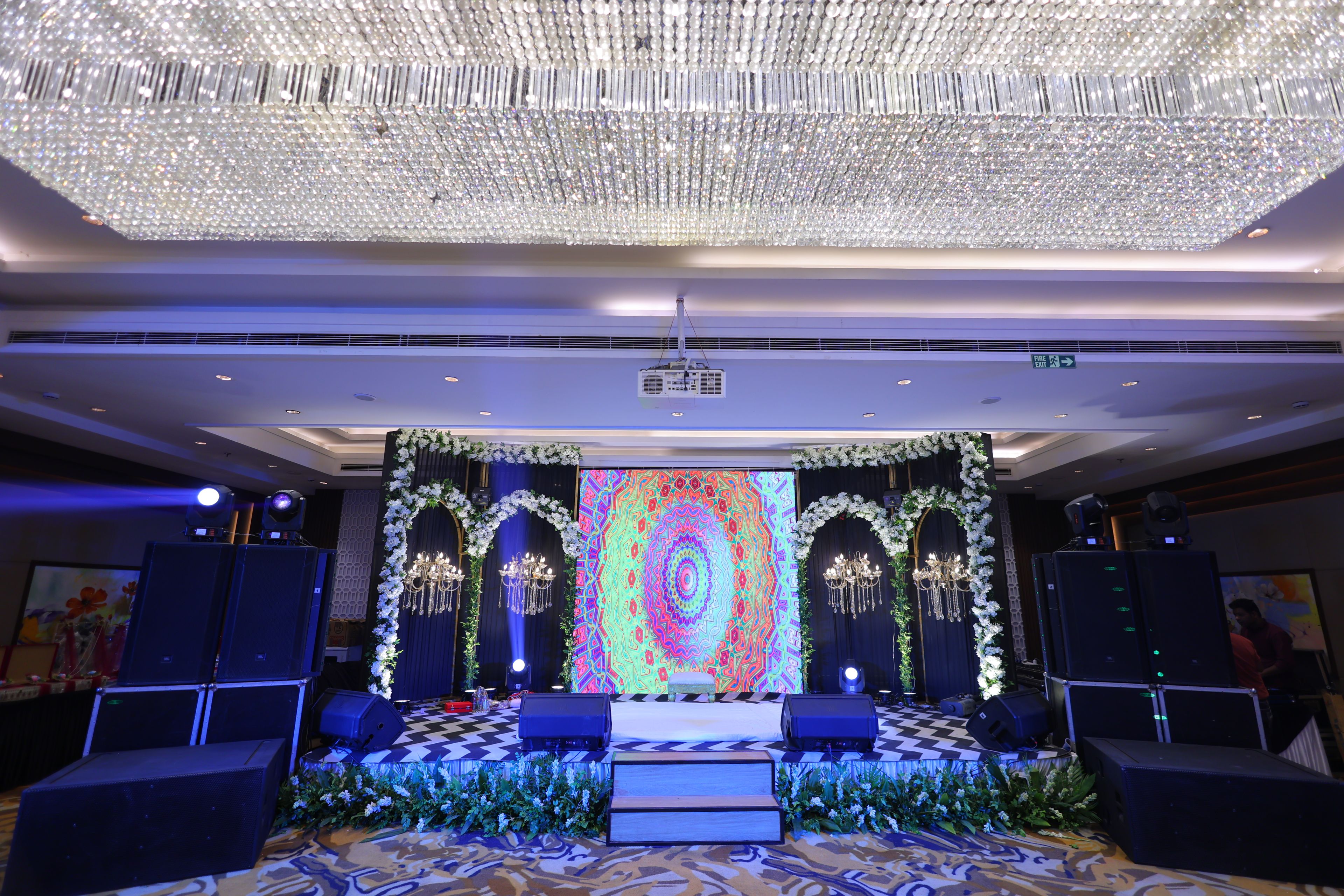 A stage with a colorful LED backdrop, floral decorations, and a chandelier.