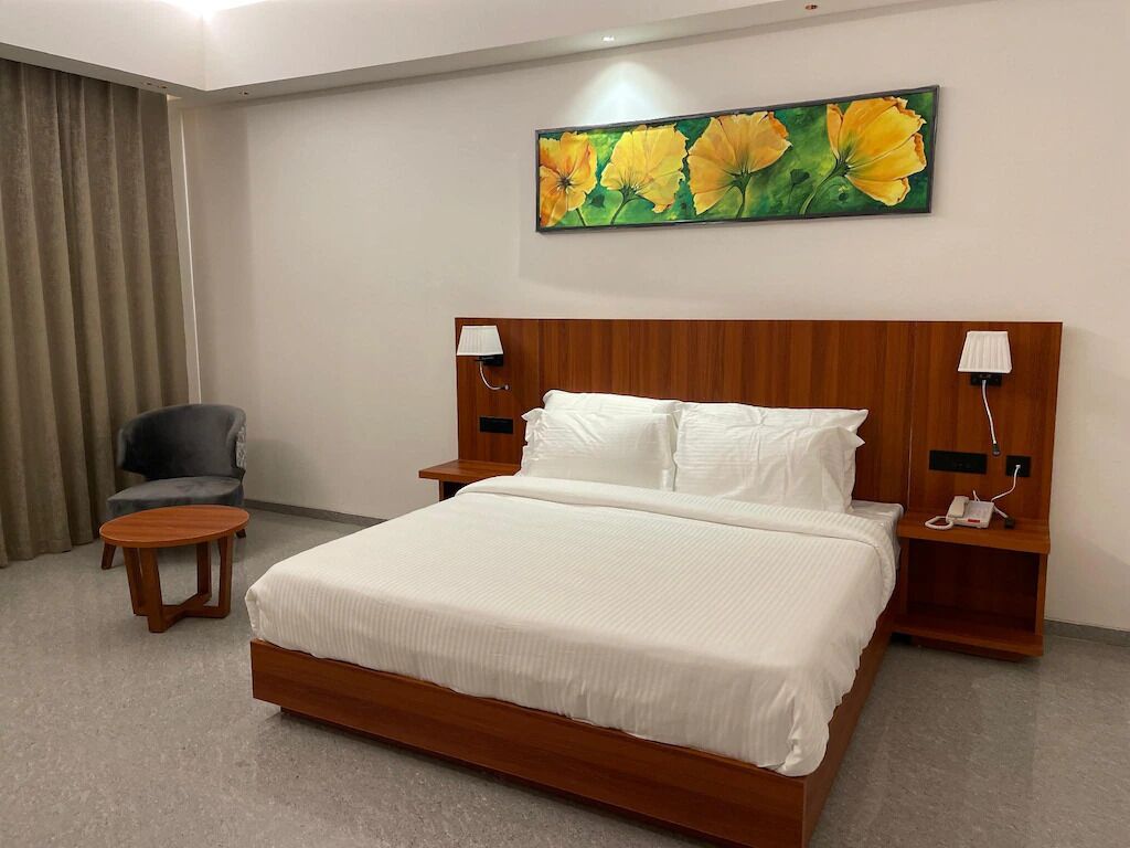 A hotel room with a large bed, two bedside tables, a chair, and a painting of flowers on the wall.