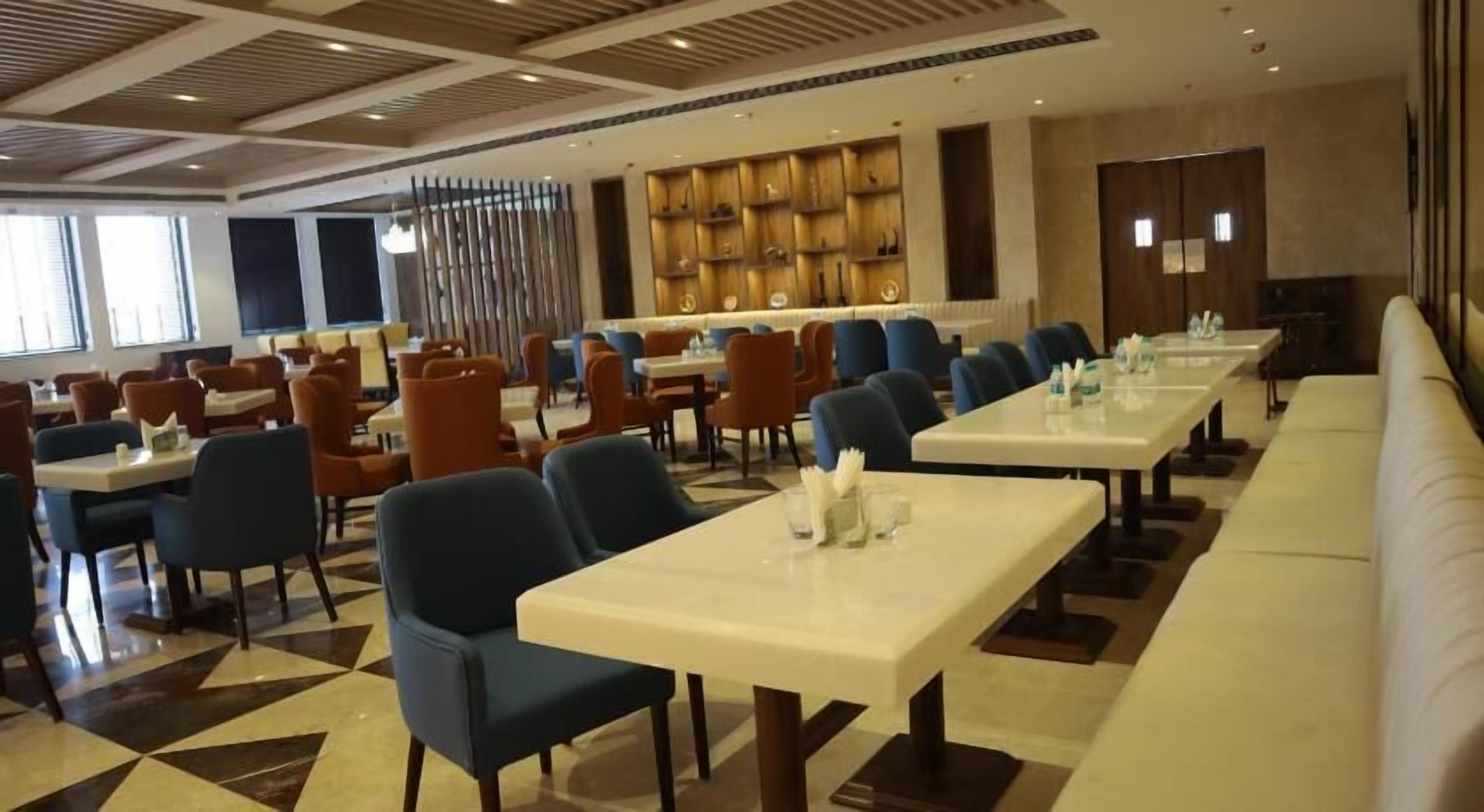 Un comedor espacioso con varias mesas y sillas, una barra alargada y una pared decorativa con estantes.