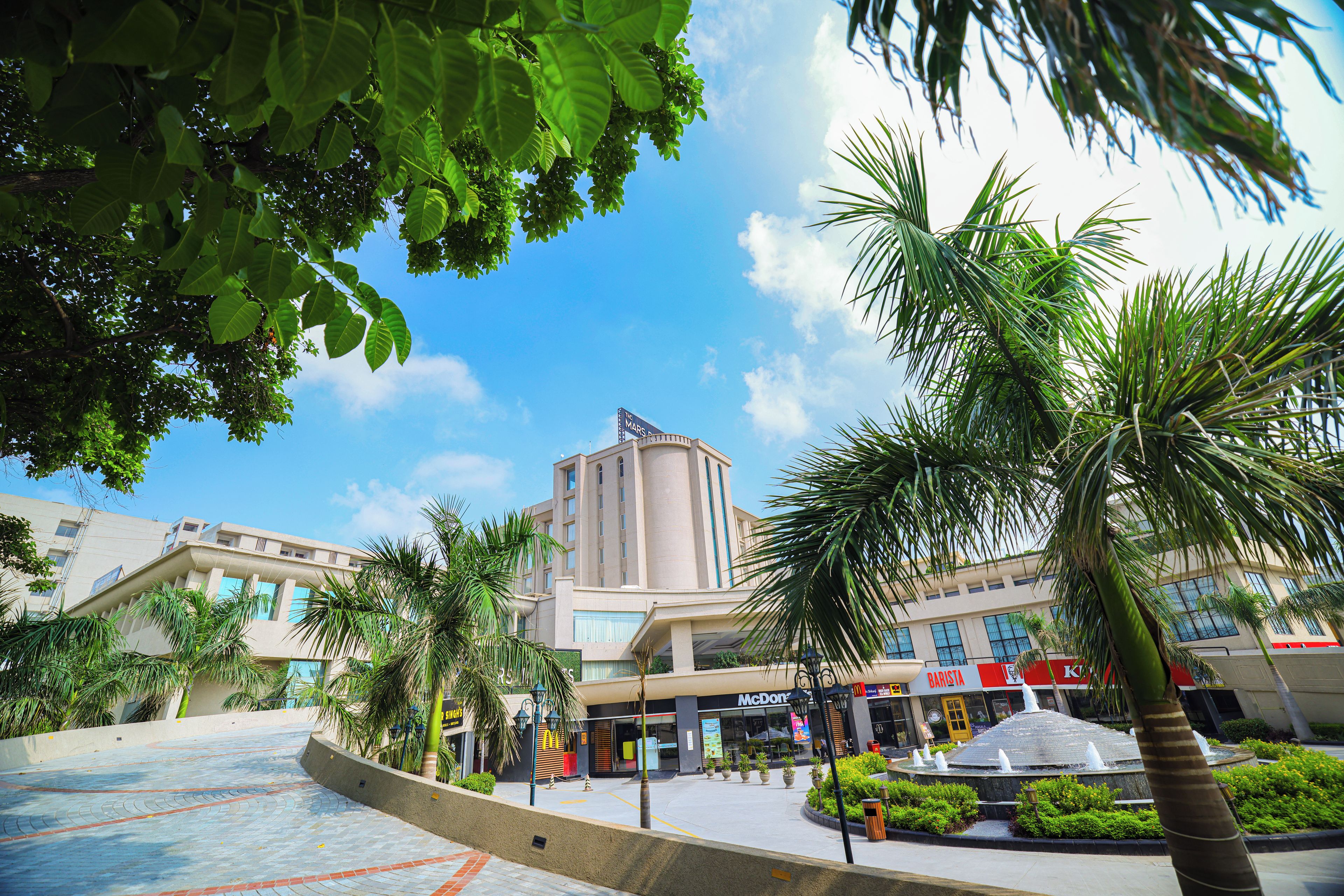 A plaza with a fountain, palm trees, and a building with a sign that reads 'McDonald's'.