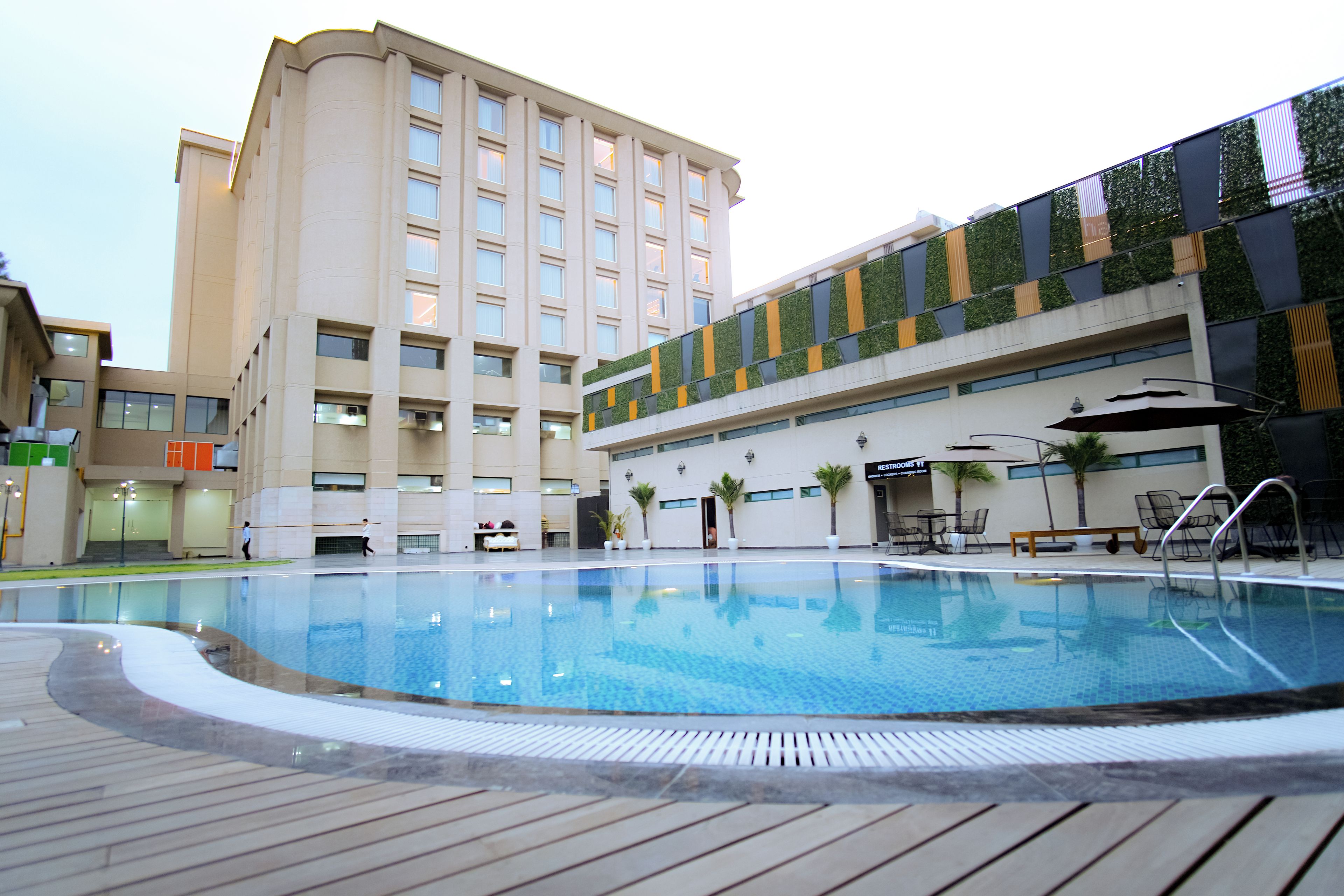 A swimming pool with a wooden deck, a hotel building with multiple floors and balconies, and a sign for 'RESTRICTED ROOMS'.