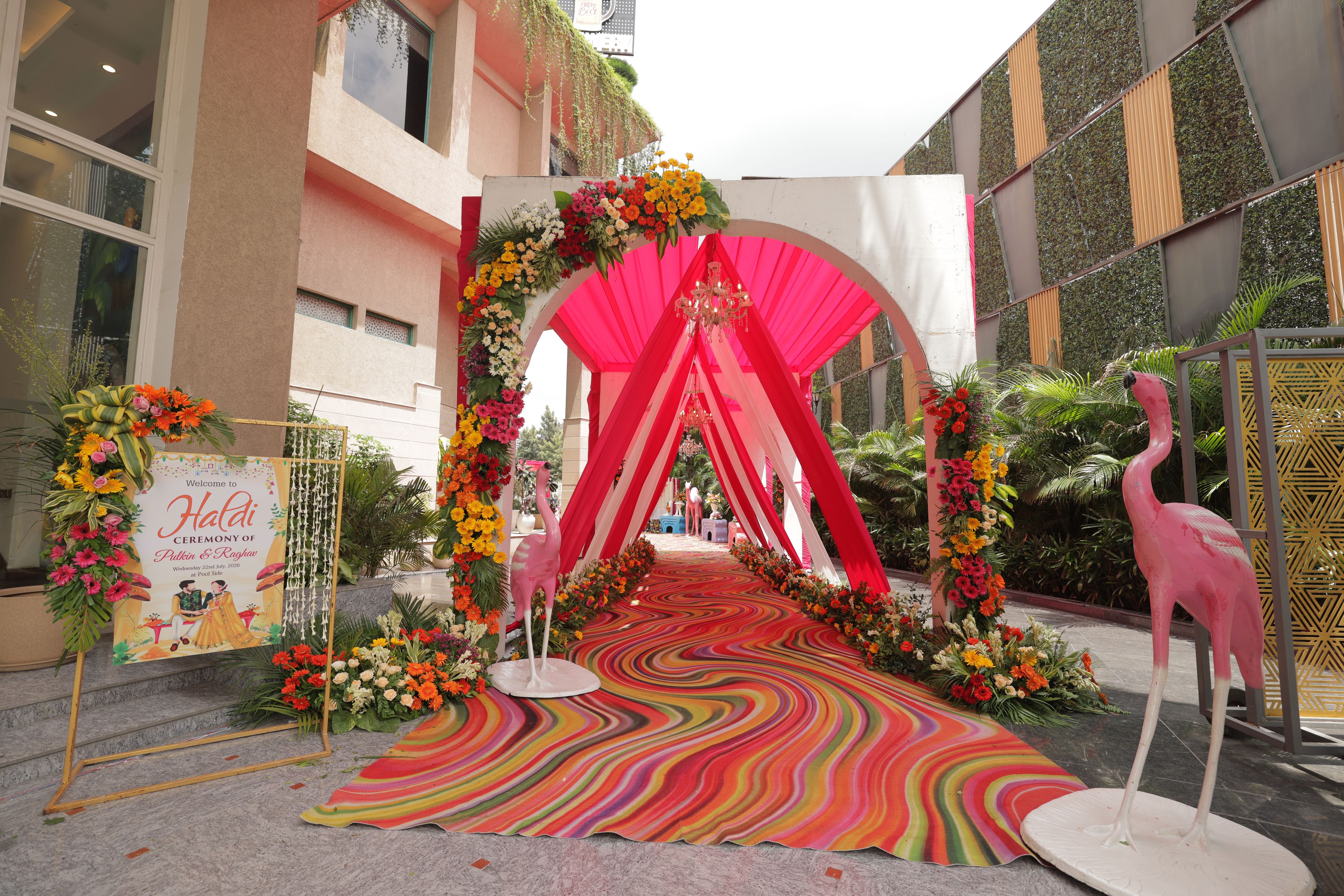 A decorated entrance with a colorful carpet, floral arrangements, and a pink archway.