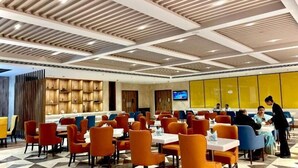 A modern dining area with orange and blue chairs, a checkered floor, and a TV on the wall. - Mars Resorts (Meerut)