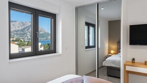 Ein Schlafzimmer mit Bett, Nachttisch, Fernseher und Blick auf Berg und Meer.