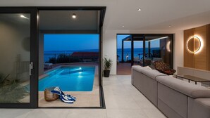 Ein modernes Wohnzimmer mit Pool, einer Couch und Meerblick.