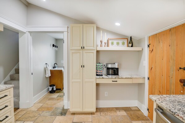A compact kitchen with a built-in oven, a coffee maker, and a shelf with decorative items.