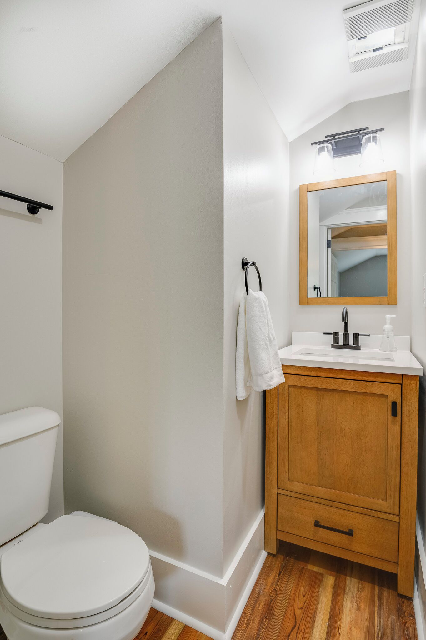 Une salle de bain avec des toilettes blanches, un meuble-lavabo en bois et un miroir au-dessus du lavabo.