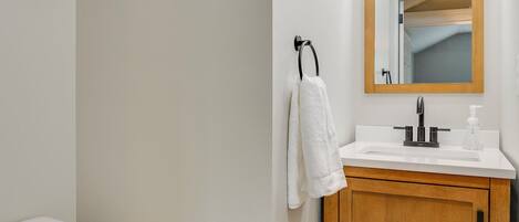 Een badkamer met een wit toilet, een houten wastafelmeubel en een spiegel boven de wastafel.