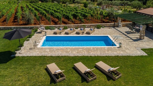 Una piscina rectangular amb un marc de pedra, envoltada per un prat verd i una pèrgola.