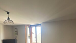 A living room with a large window, a flat-screen TV, a sofa, and a ceiling fan. - Spacieux Appartement sur la Murette (La Murette)