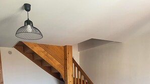 A room with a wooden staircase, a round table with chairs, and a hanging light fixture. - Spacieux Appartement sur la Murette (La Murette)