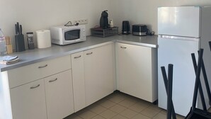 A small, clean kitchen with white cabinets, a microwave, a coffee maker, and a refrigerator. - Spacieux Appartement sur la Murette (La Murette)