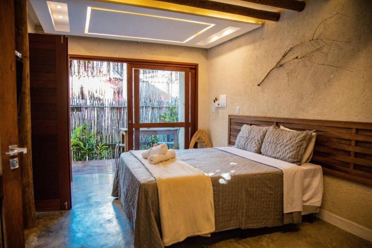 Un dormitorio con cama, cabecera de madera, ventana y vista a una valla de bambú.