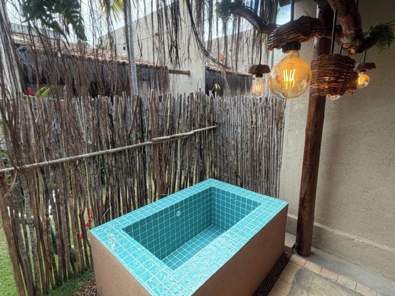 Eine rechteckige Freiluftbadewanne mit blauen Fliesen, umgeben von einem Holzzaun und einer Mauer.