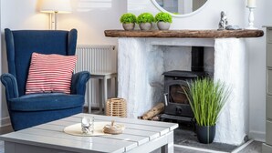 A cozy living room with a blue armchair, a white coffee table, a fireplace, and a mirror on the wall. - Norton Cottage - 3 Bedroom Cottage - Tenby (Tenby)