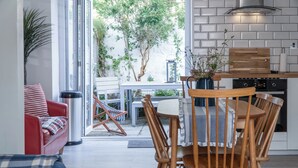 A modern kitchen with a wooden table and chairs, a red sofa, and a large window overlooking a garden. - Norton Cottage - 3 Bedroom Cottage - Tenby (Tenby)