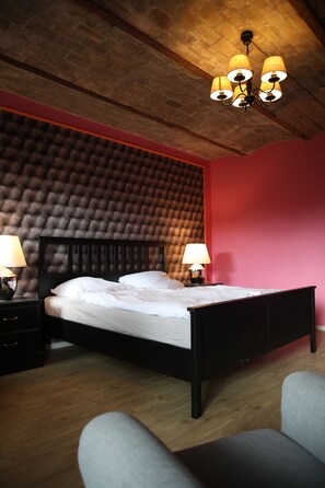 Un dormitorio con cabecera capitonada, cama con ropa de cama blanca, dos lámparas de noche y techo de madera con candelabro.