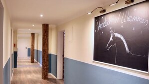 A hallway with wooden flooring, blue walls, and a large wall mural featuring a horse and the text "Herzlich Willkommen". - Hotel Hof Kirchhorst (Gross Wittensee)