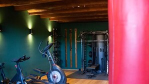 A gym with exercise bikes, a weightlifting station, and wooden flooring. - Hotel Hof Kirchhorst (Gross Wittensee)