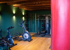 Ein Fitnessraum mit Ergometer, einer Gewichthebezone und Holzböden.
