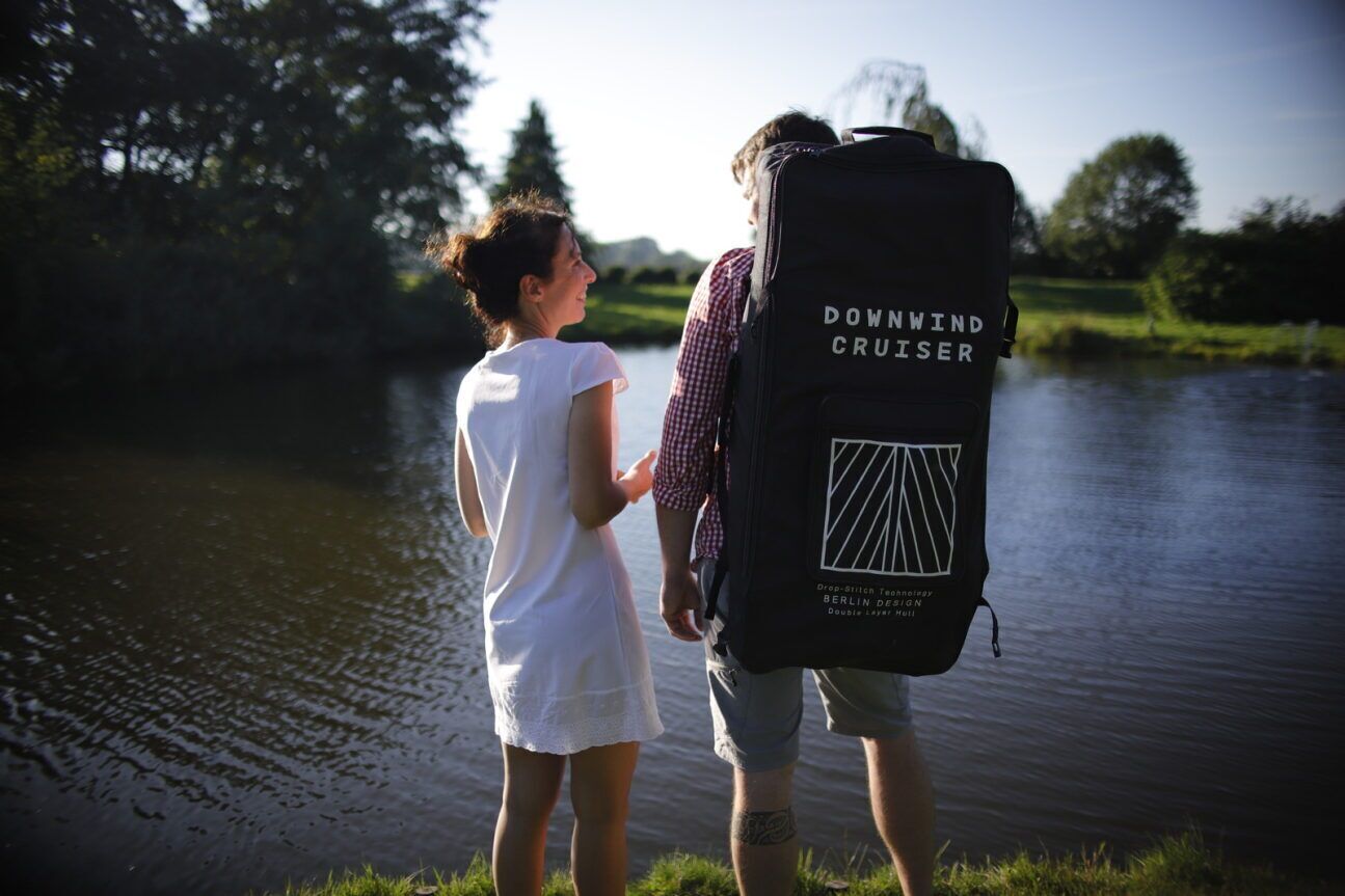 A couple standing by a lake with a large backpack labeled "Downwind Cruiser" on the back.