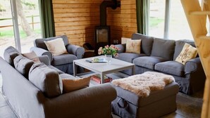 A cozy living room with a fireplace, grey sofas, and a coffee table with a vase of flowers. - Hotel Hof Kirchhorst (Gross Wittensee)