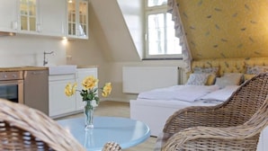 A cozy bedroom with a bed, a wicker chair, and a vase with flowers on a small table. - Hotel Hof Kirchhorst (Gross Wittensee)