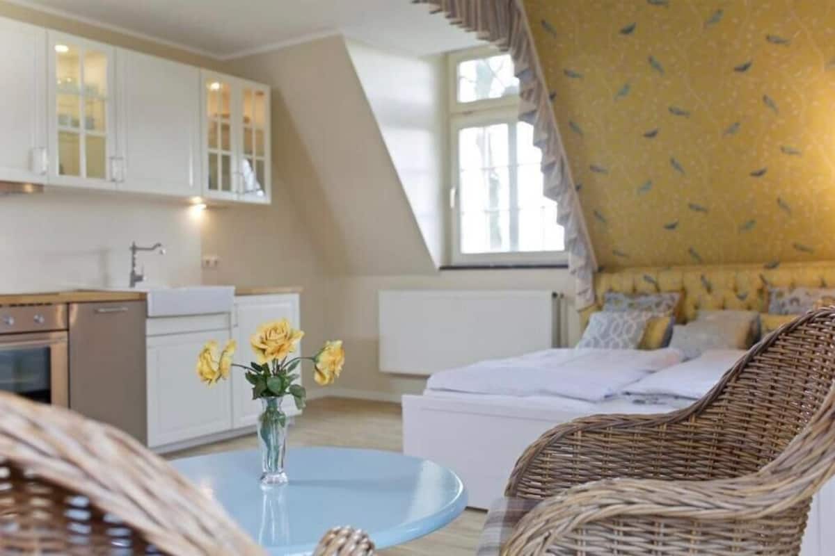 Une chambre confortable avec un lit, un fauteuil en osier et un vase de fleurs posé sur une petite table.