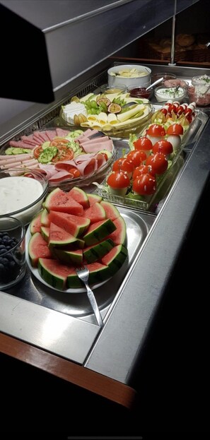 Un bufé con diferentes opciones de comida, incluyendo sandía en rodajas, tomates cherry y distintos tipos de queso.