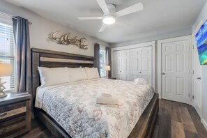 Quarto com uma cama grande, um ventilador de teto, mesa de cabeceira, abajur e uma obra de arte na parede.